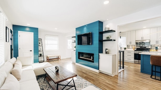 Una sala de estar moderna con chimenea, comedor y cocina con armarios blancos y detalles en azul.