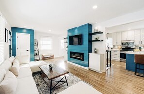 Un salon moderne doté d’une cheminée, d’un coin repas et d’une cuisine avec des meubles blancs et des touches de bleu.