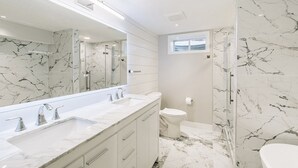 Un baño moderno con un espejo grande, dos lavamanos, un inodoro y una zona de ducha.