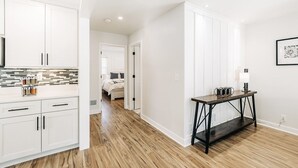 Una cocina moderna con armarios blancos, piso de madera y un comedor con mesa de madera oscura.