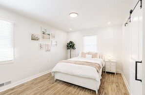 Une chambre à coucher avec un lit, des tables de chevet, une plante et des œuvres d’art mural.