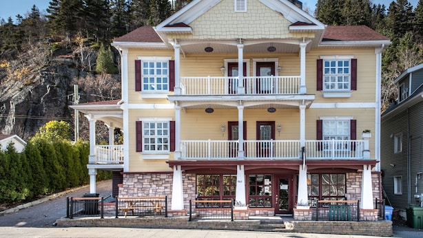 Un bâtiment à deux étages doté d’un balcon, de fondations en pierre et d’une porte rouge.