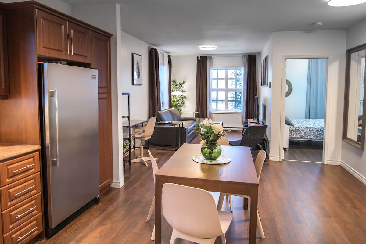 A modern kitchen with a built-in refrigerator, a dining area with a wooden table and chairs, and a living room with a sofa and a TV.