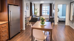 Une cuisine moderne dotée d’un réfrigérateur encastré, un coin repas avec une table et des chaises en bois, et un salon avec un canapé et un téléviseur.