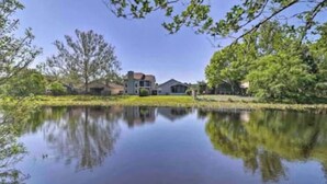A house with a reflection in a calm body of water, surrounded by trees and a clear sky.