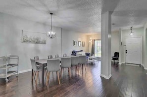 Un salón amplio con comedor, pisos de madera y una araña.