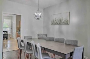 Un comedor moderno con una mesa larga y seis sillas, una araña y una obra de arte enmarcada en la pared.