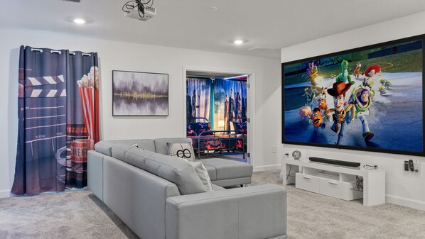 A modern living room with a grey sectional sofa, a flat-screen TV, and a projector.