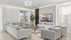 A modern living room with a grey sofa, a glass coffee table, and a TV mounted on the wall displaying various shows.