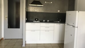 Cocina compacta con armarios blancos, campana extractora de acero inoxidable, pileta y refrigerador blanco.