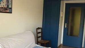 Una habitación con un sofá blanco, una silla de madera pequeña, una puerta azul y un cuadro en la pared.