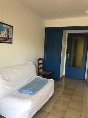 A room with a white sofa, a small wooden chair, a blue door, and a painting on the wall.