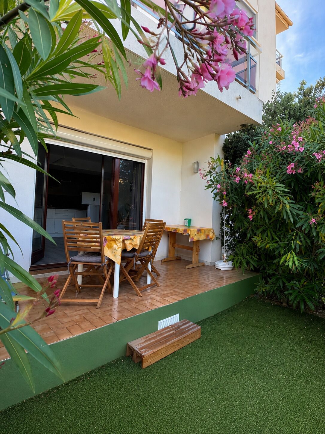 Une terrasse avec une table et des chaises, un petit jardin et un bâtiment doté d’une porte-fenêtre coulissante.