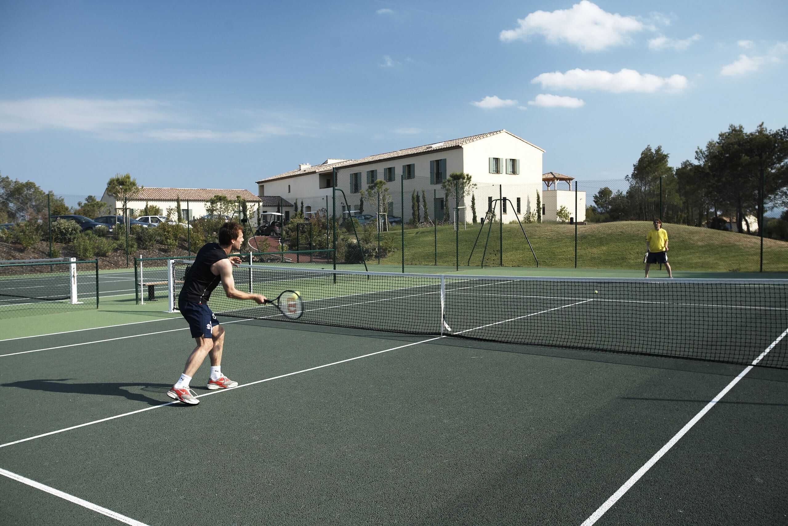A tennis court with a net in the middle, surrounded by a fence.