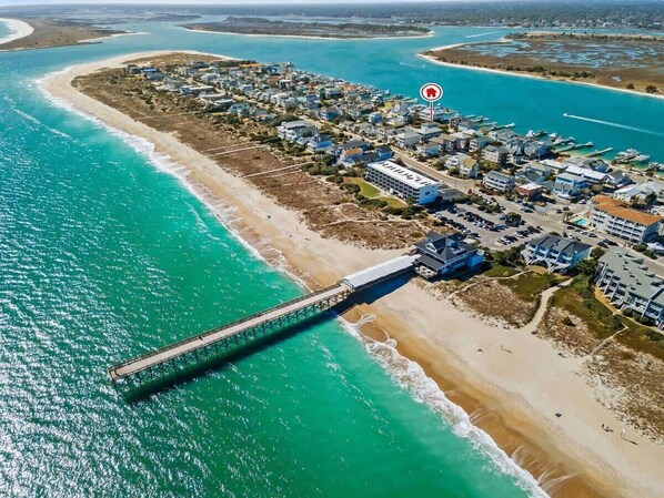 An aerial view of a coastal area with a pier, beachfront properties, and a marina.