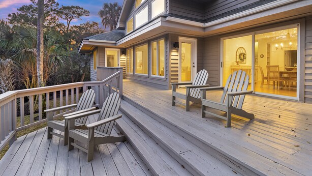 A wooden deck with Adirondack chairs, a covered area with glass doors, and a view of the surrounding landscape. - Spacious & Modern Home- Pond Views, Close to Beach (Kiawah Island)