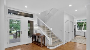 A spacious interior with a wooden floor, a white staircase, and a view of the outdoors. - Spacious & Modern Home- Pond Views, Close to Beach (Kiawah Island)
