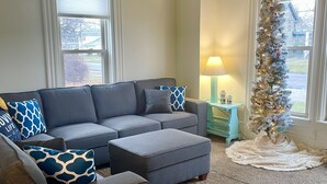 A living room with a gray sectional sofa, a small ottoman, and a Christmas tree. - Walnut Beach Inn - close to the beach! (Ashtabula)