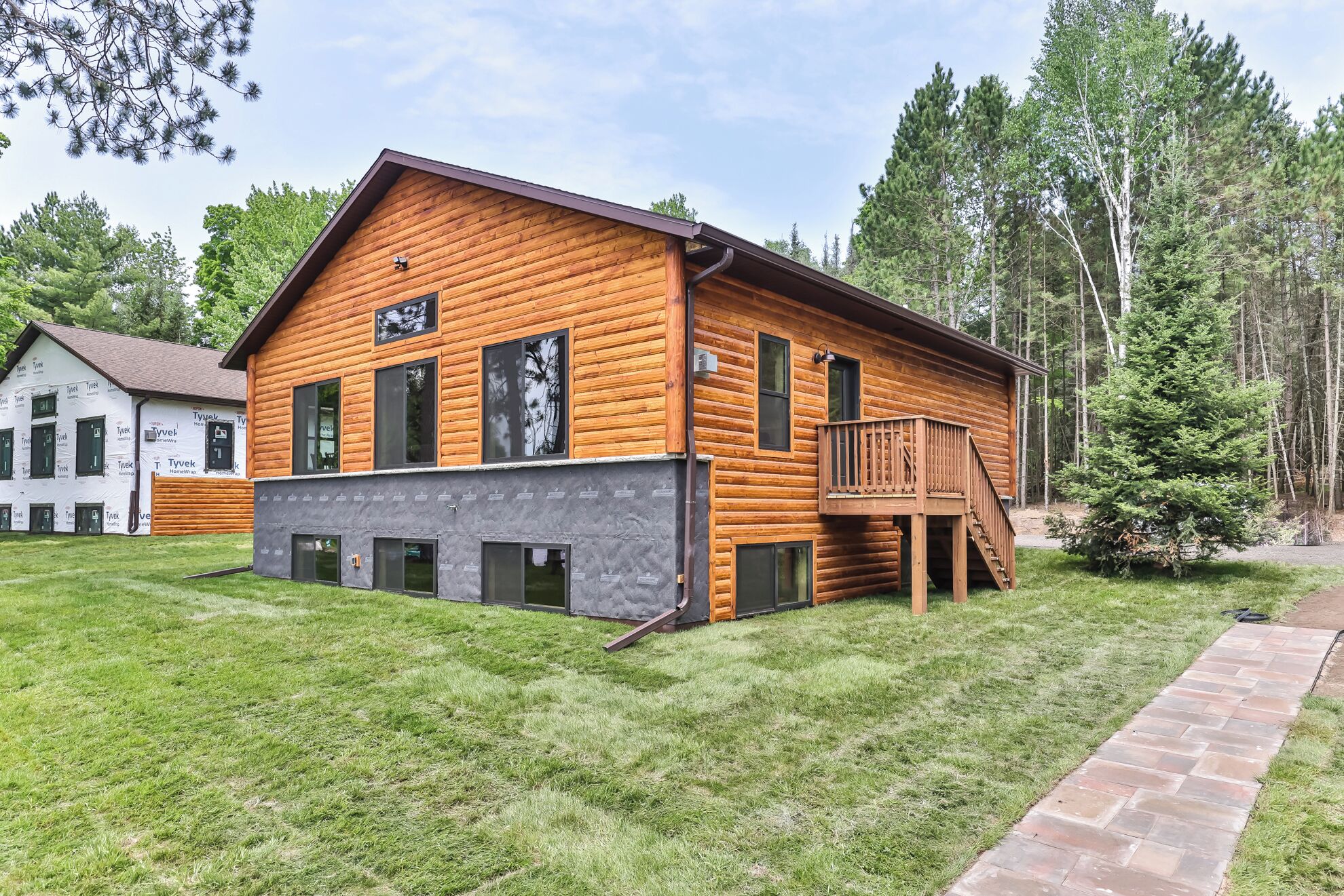 A log cabin with a balcony, a covered porch, and a brick pathway leading to the entrance.