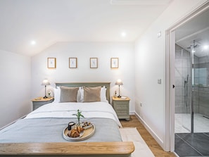 A neatly arranged bedroom with a bed, bedside tables, a tray with pastries, and a shower area.