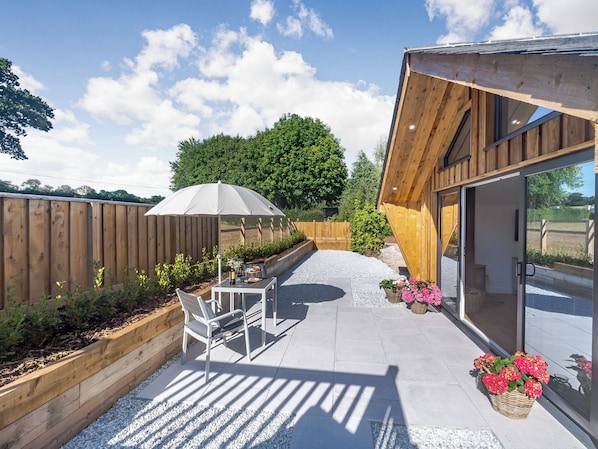 A patio with a table and chairs, a wooden fence, and a building with a glass door.
