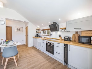 A modern kitchen with white cabinetry, a wooden countertop, a built-in oven, a microwave, and a dining area with a table and chairs.