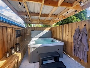 A wooden deck with a hot tub, a bench, and towels hanging on the wall.