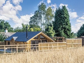 A wooden cabin with a sloped roof, a chimney, and a fenced yard.