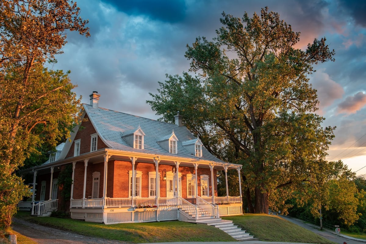 A large, two-story brick house with a wrap-around porch and a chimney.