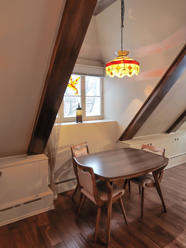 Un comedor con una mesa y sillas de madera, una lámpara colgante y una ventana con vistas a árboles.