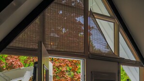 A room with a large window, a door, and a view of a deck with chairs and a table. - Appartement Jacques-Cartier (Saguenay)