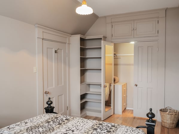 A bedroom with a bed, a closet with open doors, and a small table with a lamp. - Appartement Jacques-Cartier (Saguenay)