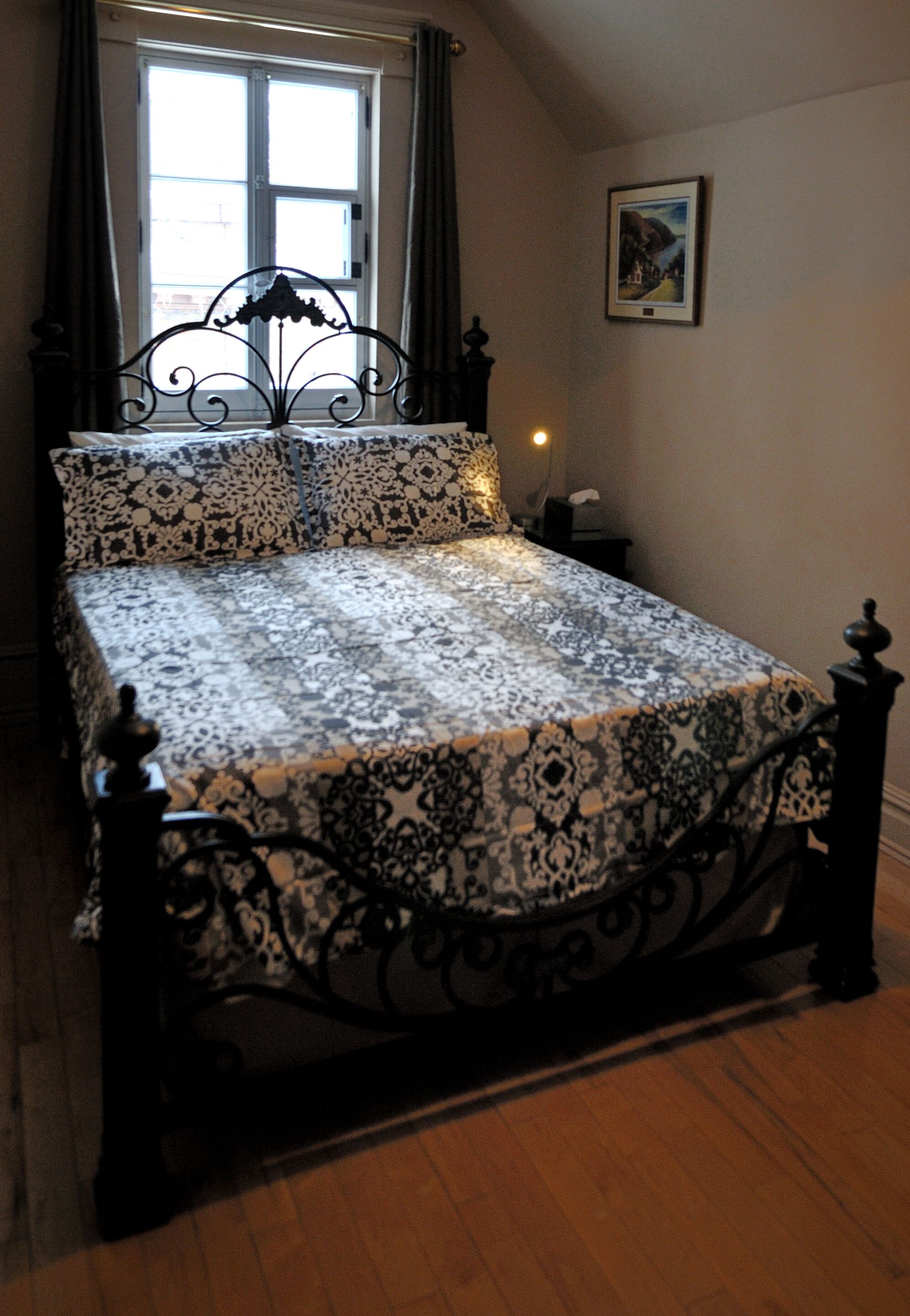 A bed with a patterned bedspread, a window with curtains, and a framed picture on the wall.