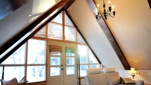 A cozy room with a sloped ceiling, a cushioned sofa, a chair, and a table with a lamp. - Appartement Jacques-Cartier (Saguenay)