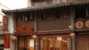 A traditional wooden building with a signboard, a tiled roof, and a wooden door with glass panels. - Pailou Guesthouse (Yueqing)