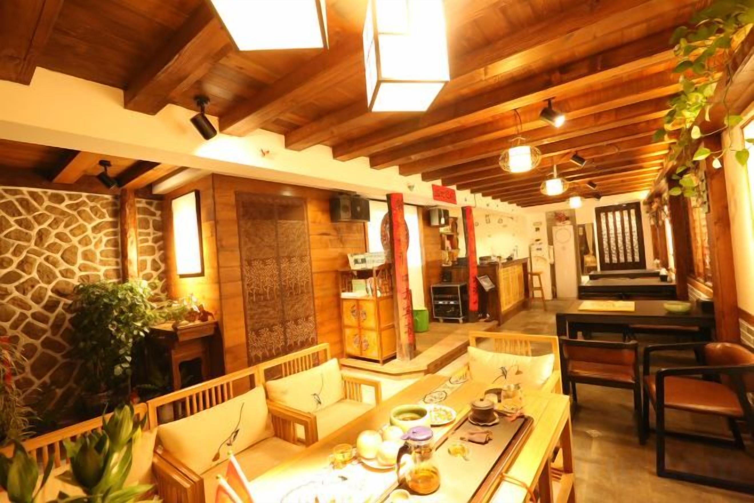Ein gemütliches Interieur mit Holzbalkendecke, Steinwand und einem Essbereich mit langem Tisch und Stühlen.