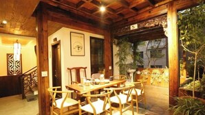 A wooden dining area with a table and chairs, a staircase, and a view of the outside. - Pailou Guesthouse (Yueqing)