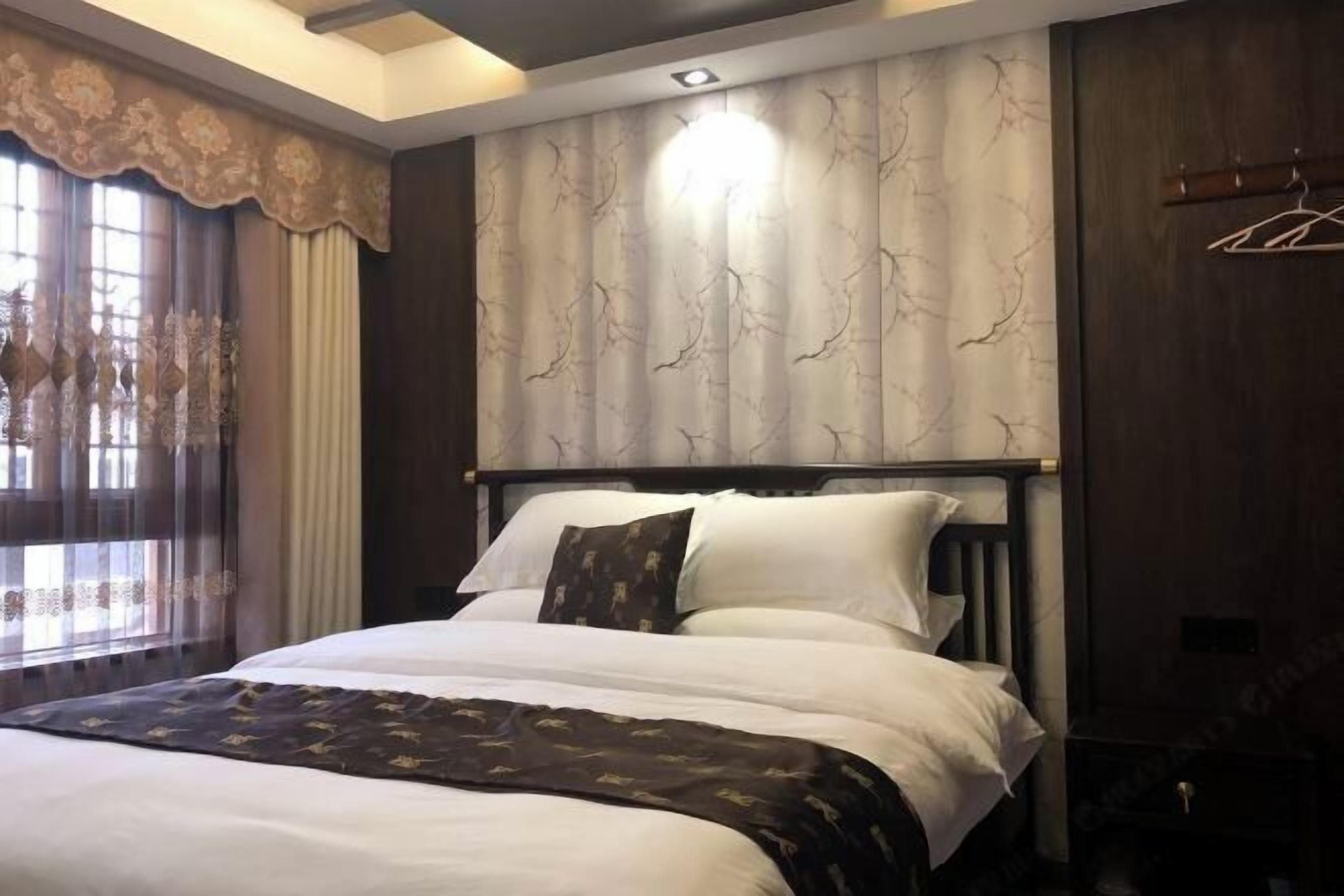 Quarto com cama grande, cabeceira de madeira escura e parede estampada.