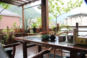 A wooden dining table with chairs, potted plants, and a view of a mountain and buildings. - Pailou Guesthouse (Yueqing)
