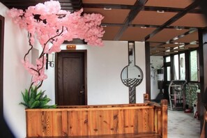 A reception area with a wooden bench, a door, and a large pink flowering plant. - Pailou Guesthouse (Yueqing)