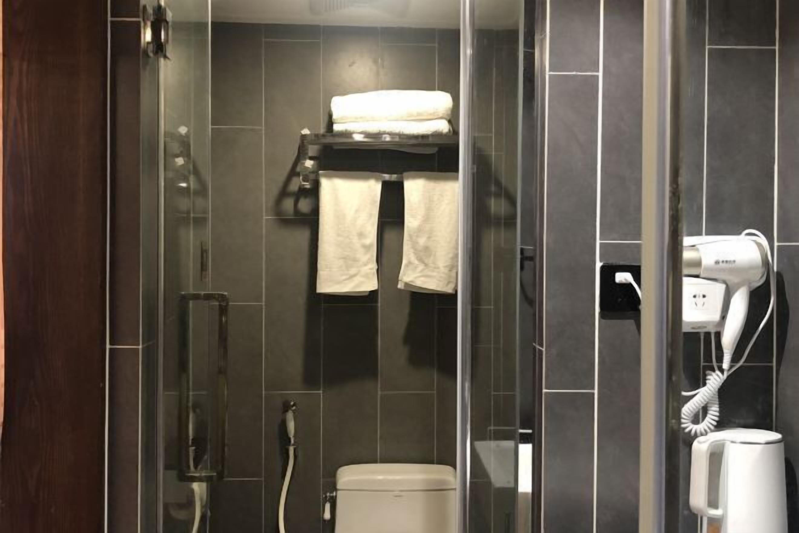 A modern bathroom with a glass shower enclosure, a toilet, a towel rack with towels, and a hairdryer on the wall.