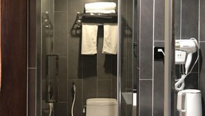 A modern bathroom with a glass shower enclosure, a toilet, a towel rack with towels, and a hairdryer on the wall. - Pailou Guesthouse (Yueqing)