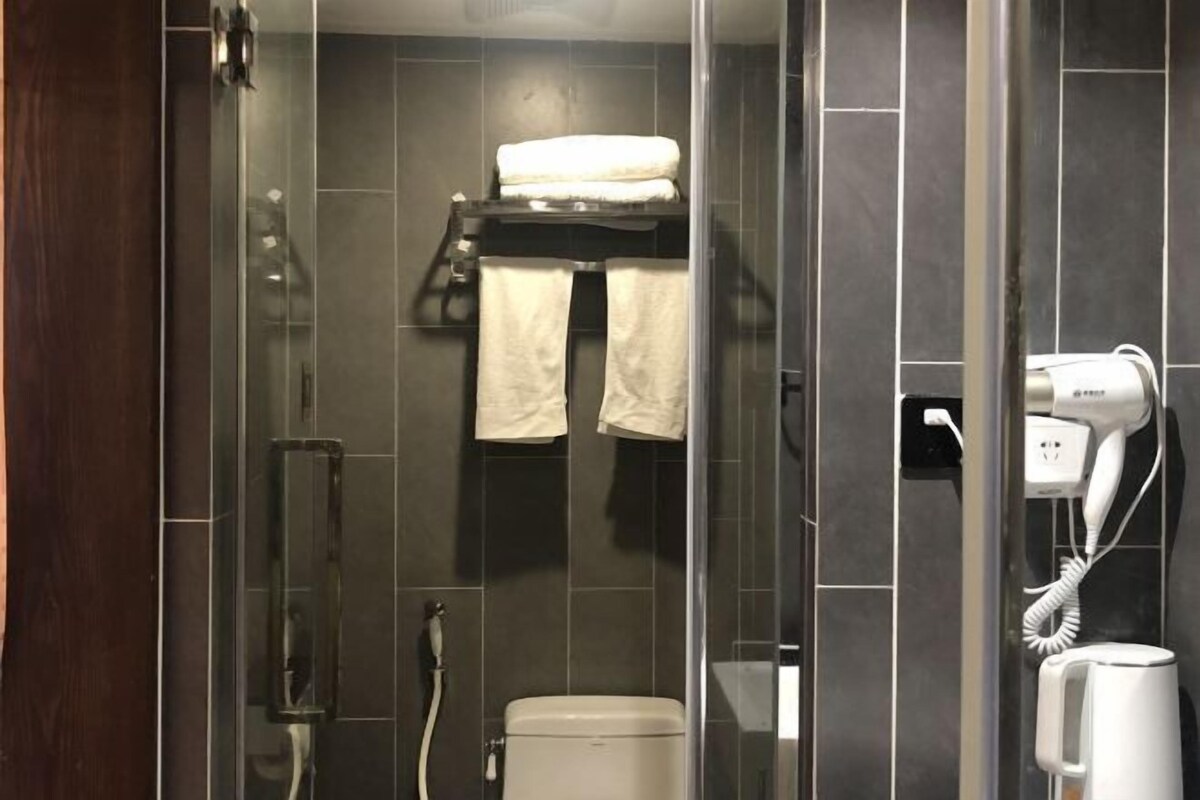 A modern bathroom with a glass shower enclosure, a toilet, a towel rack with towels, and a hairdryer on the wall.