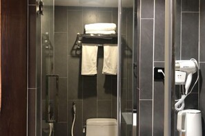A modern bathroom with a glass shower enclosure, a toilet, a towel rack with towels, and a hairdryer on the wall. - Pailou Guesthouse (Yueqing)