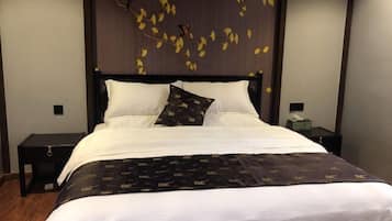 A neatly made bed with white linens and a dark patterned throw, a wooden headboard with leaf decorations, and a small bedside table with a lamp.