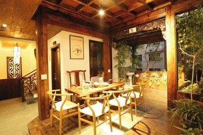 A wooden dining area with a table and chairs, a staircase, and a view of greenery outside. - Pailou Guesthouse (Yueqing)