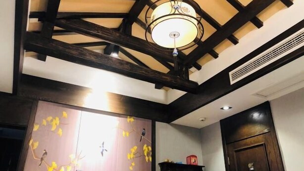 A room with exposed wooden beams, a chandelier, a wall with a bird mural, and a door with a handle. - Pailou Guesthouse (Yueqing)