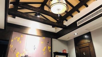A room with exposed wooden beams, a chandelier, a wall with a bird mural, and a door with a handle.