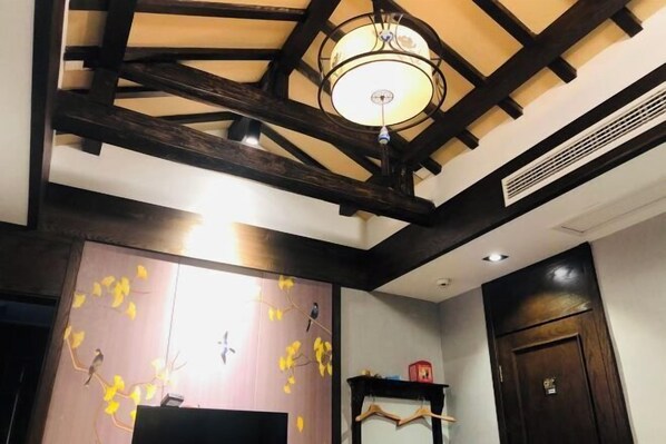 A room with exposed wooden beams, a chandelier, a wall with a bird mural, and a door with a handle. - Pailou Guesthouse (Yueqing)