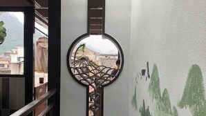 A circular decorative element with a geometric pattern, a view of buildings through a window, and a wall with green abstract designs. - Pailou Guesthouse (Yueqing)